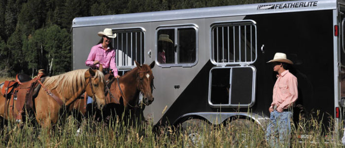 Horses being ridden in front of Featherlite horse trailer